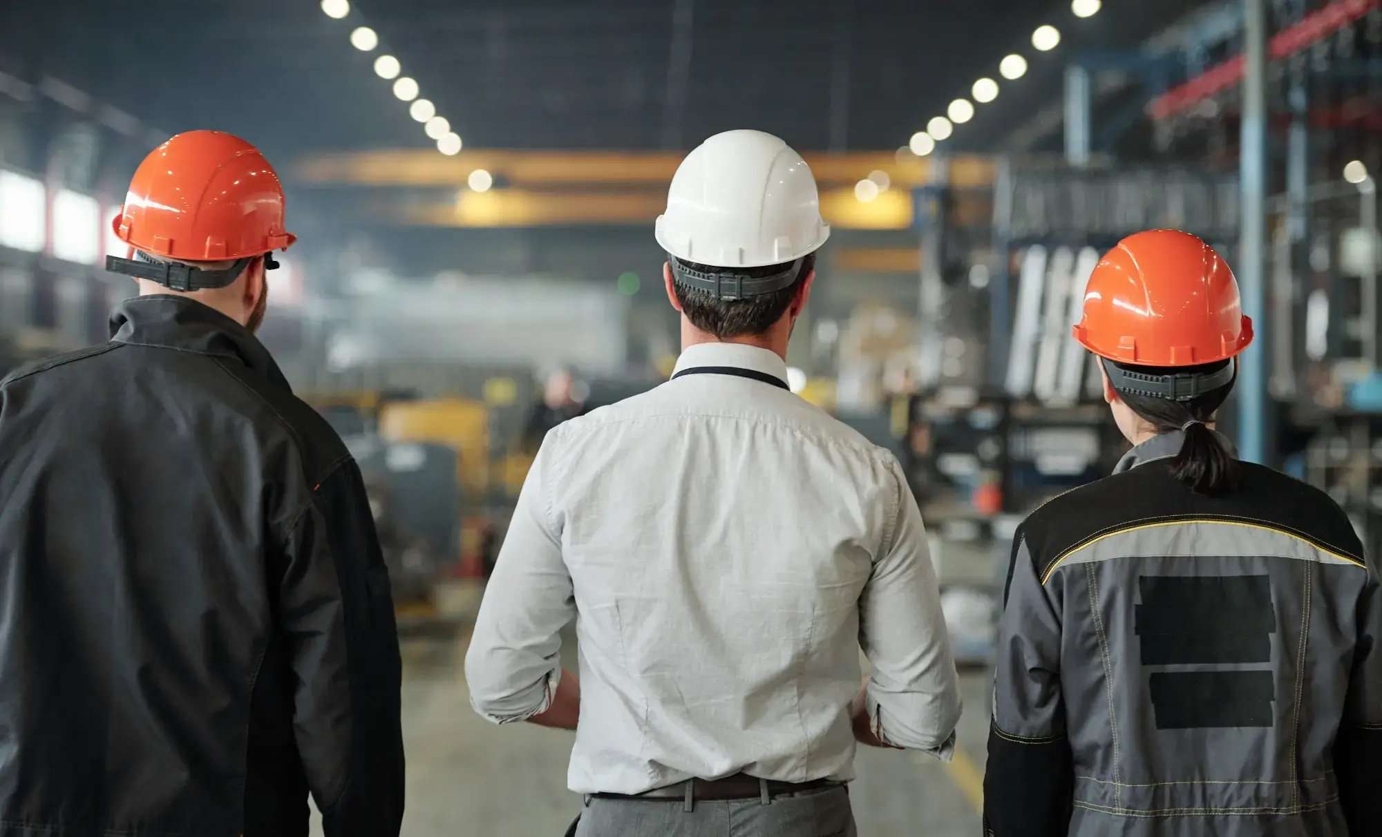 3 kollegor står med ryggen mot kameran och tittar ut i industrihallen och pratar om Likviditet för tillverkningsföretag 